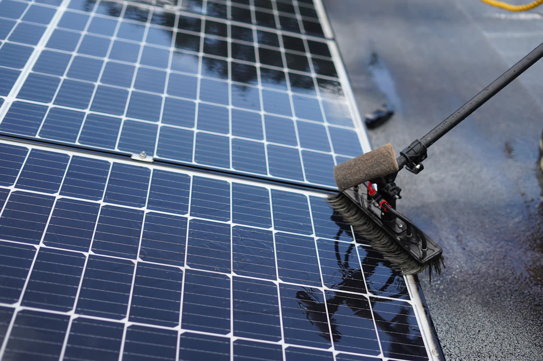 Solar panels being cleaned with a long-handled brush